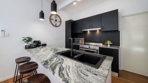 A modern kitchen with a marble island, black cabinets, and stainless steel appliances.