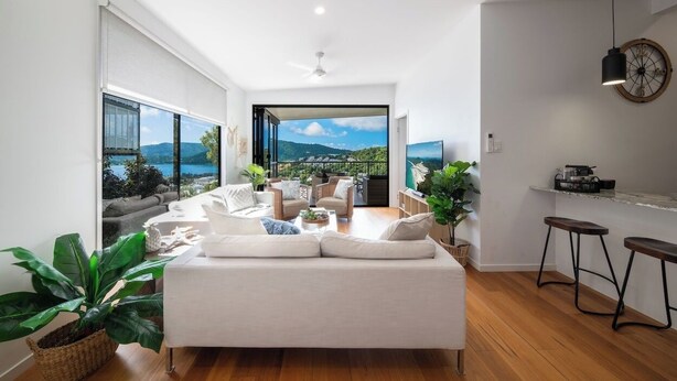 A modern living room with a large sofa, a coffee table, and a view of a mountainous landscape through large windows.