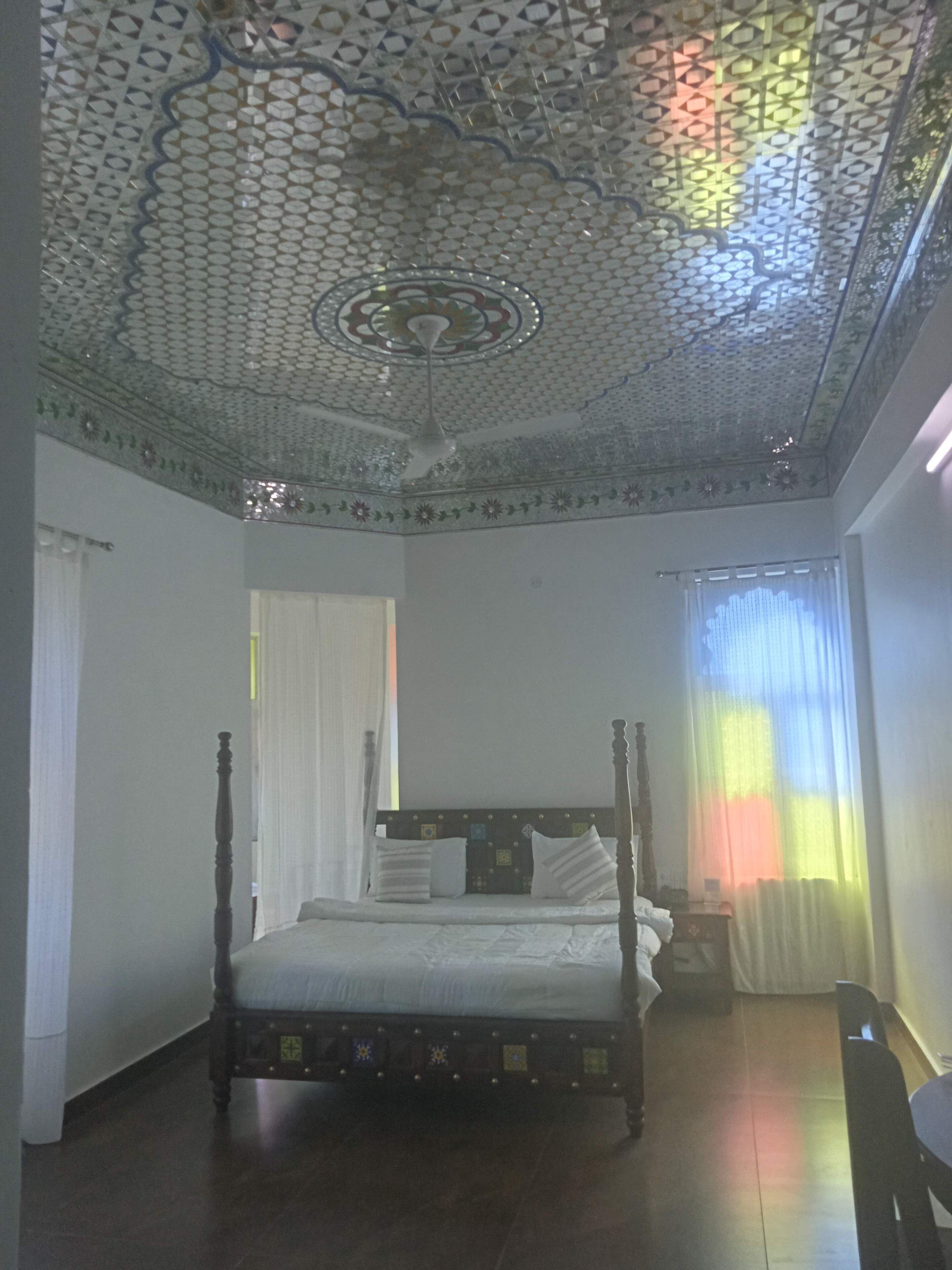 Un dormitorio con una cama con dosel, un techo decorativo y una ventana con cortinas de gasa.