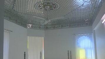 Un dormitorio con una cama con dosel, un techo decorativo y una ventana con cortinas de gasa.