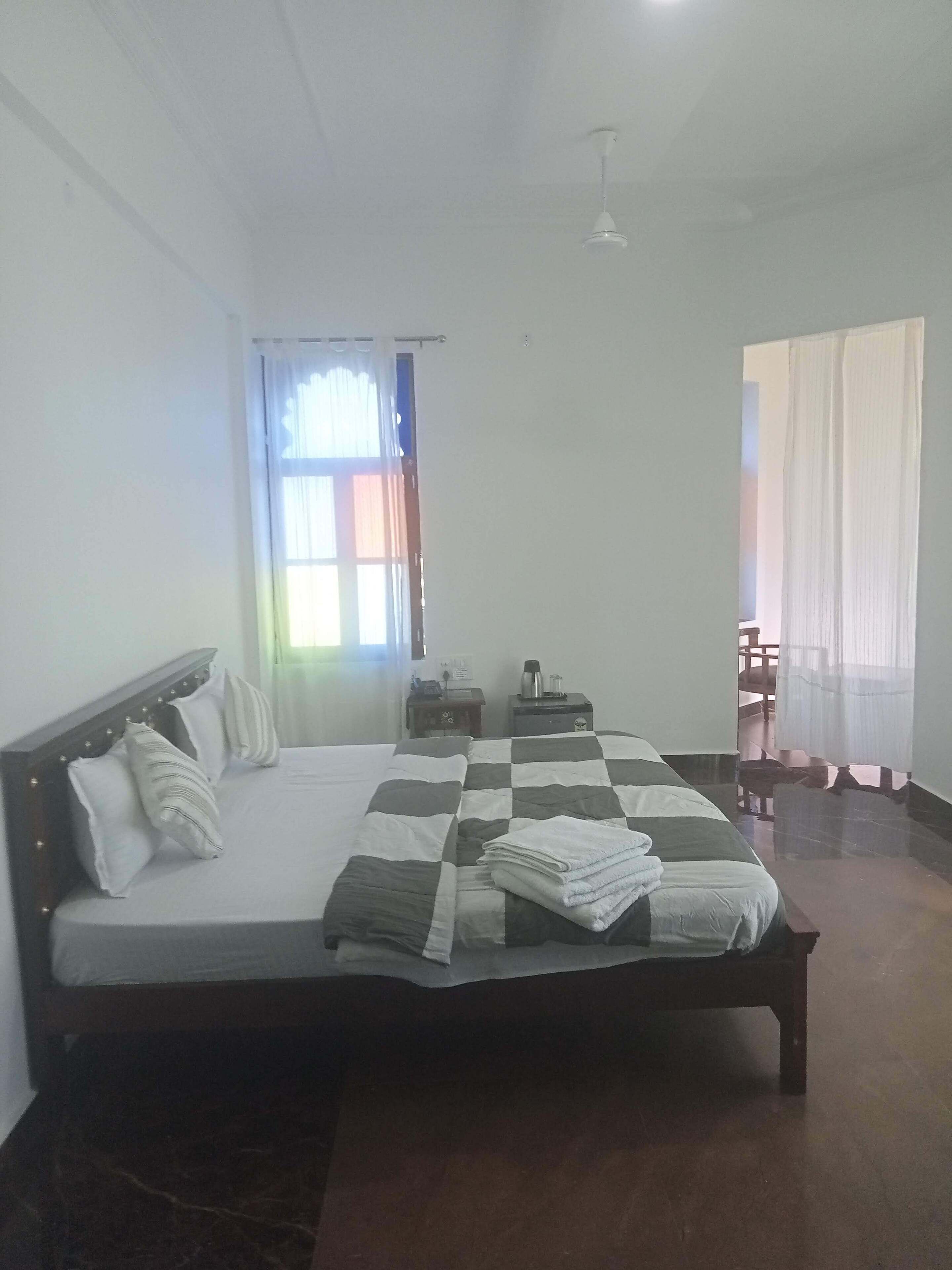 A neatly made bed with a checkered bedspread, a bedside table with a lamp, and a window with sheer curtains.