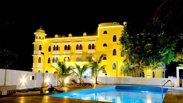 Un gran hotel con piscina, varios balcones y una fachada bien iluminada por la noche.