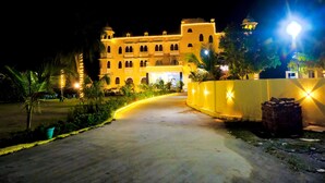 Un hotel grande y bien iluminado, con varios pisos y balcones, un camino de entrada curvo y jardines bien cuidados.
