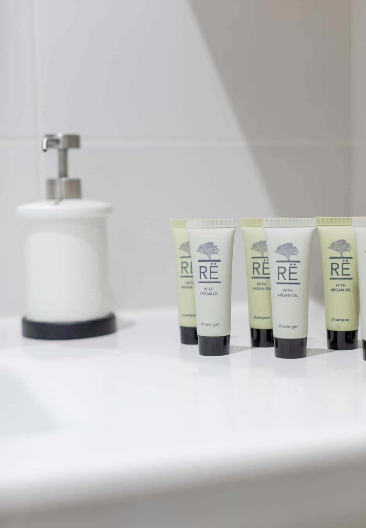 A bathroom with a white sink, a faucet, and four bottles of shower gel and shampoo.