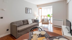 Una sala de estar moderna con un sofá gris, una mesa de comedor con platos y cubiertos, un televisor y un radiador.