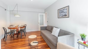 Una sala de estar moderna con comedor, un sofá gris, un cuadro en la pared y una pequeña mesa con una planta.