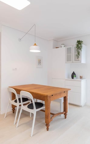 A dining area with a wooden table and white chairs, a pendant light, and a white cabinet with a plant.