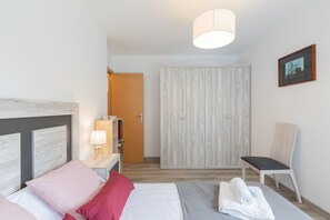 A hotel room with a bed, a bedside table with a lamp, a chair, a wardrobe, and a framed picture on the wall.