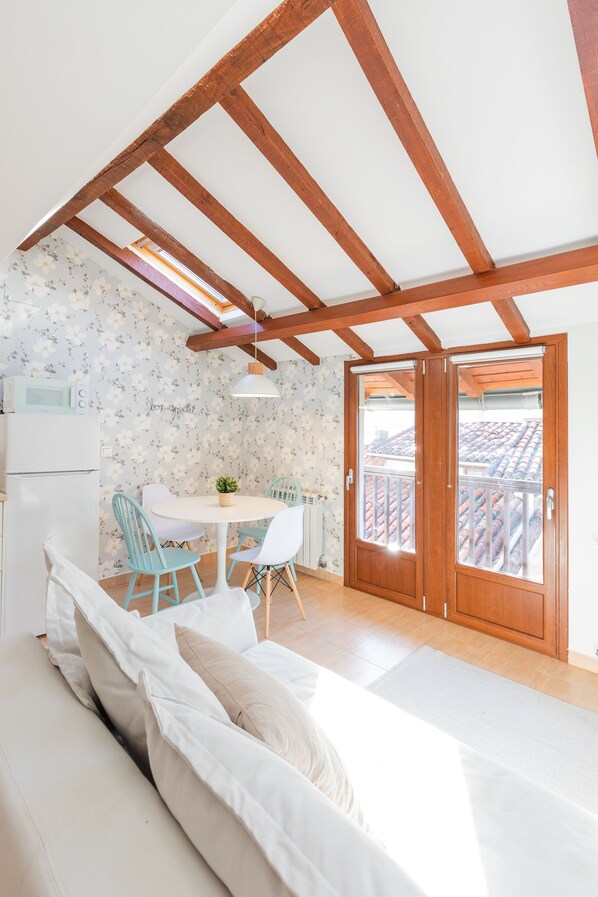 A cozy room with a bed, a dining table with chairs, a small kitchen area, and a balcony with a view.