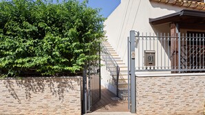 Una entrada cerrada con un muro de piedra, un portón metálico y una escalera que lleva a un edificio con un cartel con el número 91.