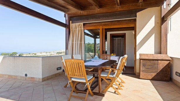 Una mesa y sillas de madera en un balcón con vista al mar.