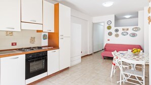 A kitchen with white cabinets, a gas stove, and a built-in oven. There is a dining area with a table and chairs, and a red sofa.