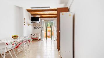 Uma sala de jantar com uma mesa posta para quatro pessoas, uma geladeira e uma cozinha visível através de uma porta aberta.