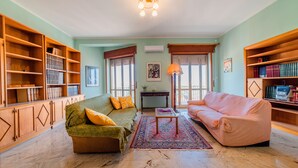 A living room with a green sofa, a pink sofa, wooden bookshelves, and a patterned rug. - La Terrazza Di Siracusa - Roomy And Bright Flat (Syracuse)