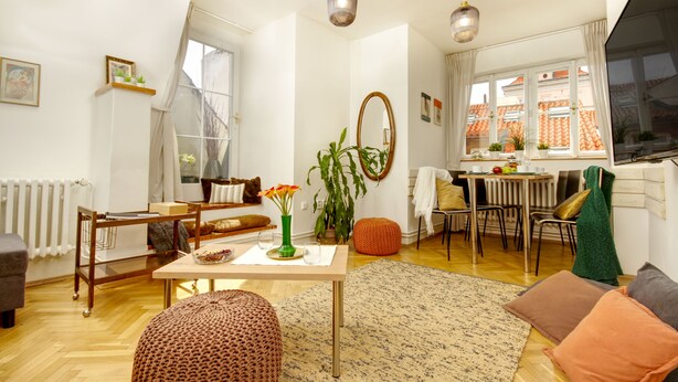 A modern living room with a wooden floor, a dining area with a table and chairs, a large window with curtains, and a radiator. - Charming APT Old Town Prague (Prague)