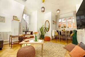 Moderni olohuone, jossa on puulattia, ruokailutila pöytineen ja tuoleineen, suuri ikkuna verhoineen ja patteri.