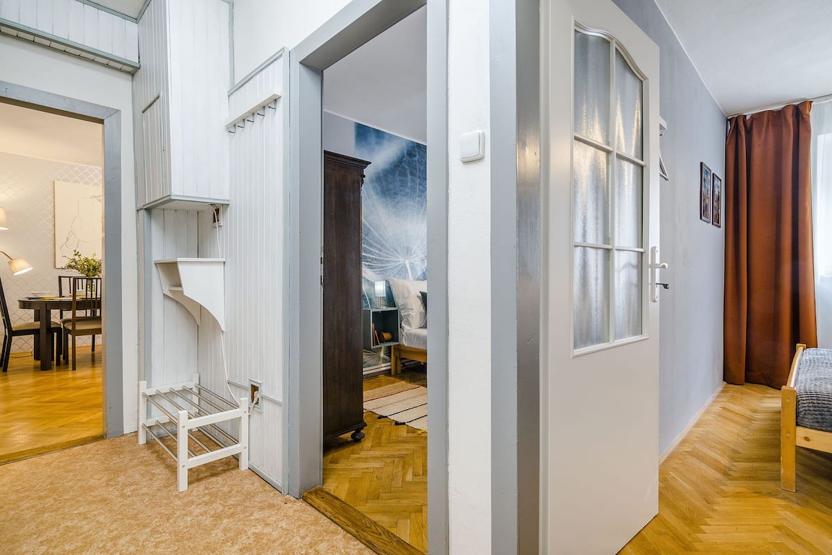 A spacious living area with a wooden floor, a white door leading to another room, and a dining area with a table and chairs.