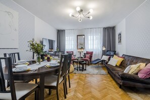 Uma sala de estar moderna com piso de madeira em padrão herringbone, um sofá de couro marrom e uma área de jantar com mesa e cadeiras de madeira.