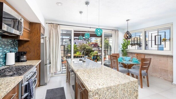 A modern kitchen with granite countertops, stainless steel appliances, and a dining area with a glass table and chairs. - Casa Turquesa - Private Pool! Local Neighbourhood (Puerto Vallarta)