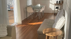 A modern living room with a sofa, a small wooden table, and a dining area with a glass table and metal chairs. - 2 Bellenger - Pet friendly two Bedroom house, located close the the beach and main street! (Nambucca Heads)