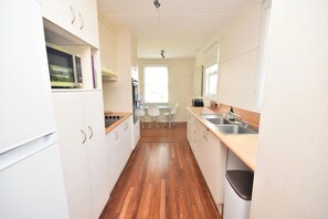 A narrow kitchen with white cabinets, a wooden countertop, a sink, and a trash bin.