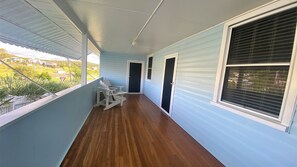 A covered porch with a wooden floor, white rocking chairs, and a view of the surrounding neighborhood.