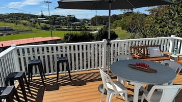 A wooden deck with a table and chairs, a white fence, and a view of a green landscape.