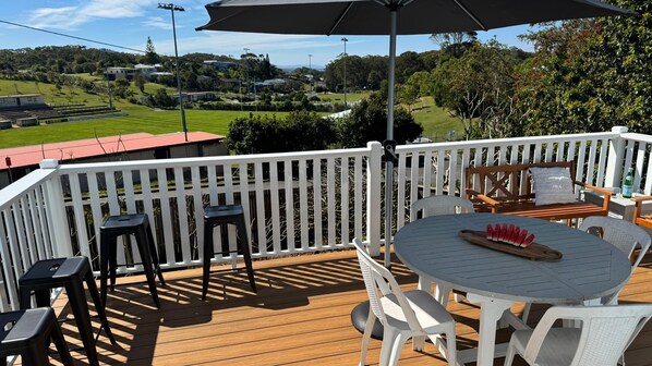 A wooden deck with a table and chairs, a white fence, and a view of a green landscape.