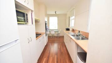 A narrow kitchen with white cabinets, a wooden countertop, a sink, and a window.