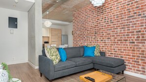 Ein modernes Wohnzimmer mit einem grauen Ecksofa, einem Glastisch und einer Ziegelwand.