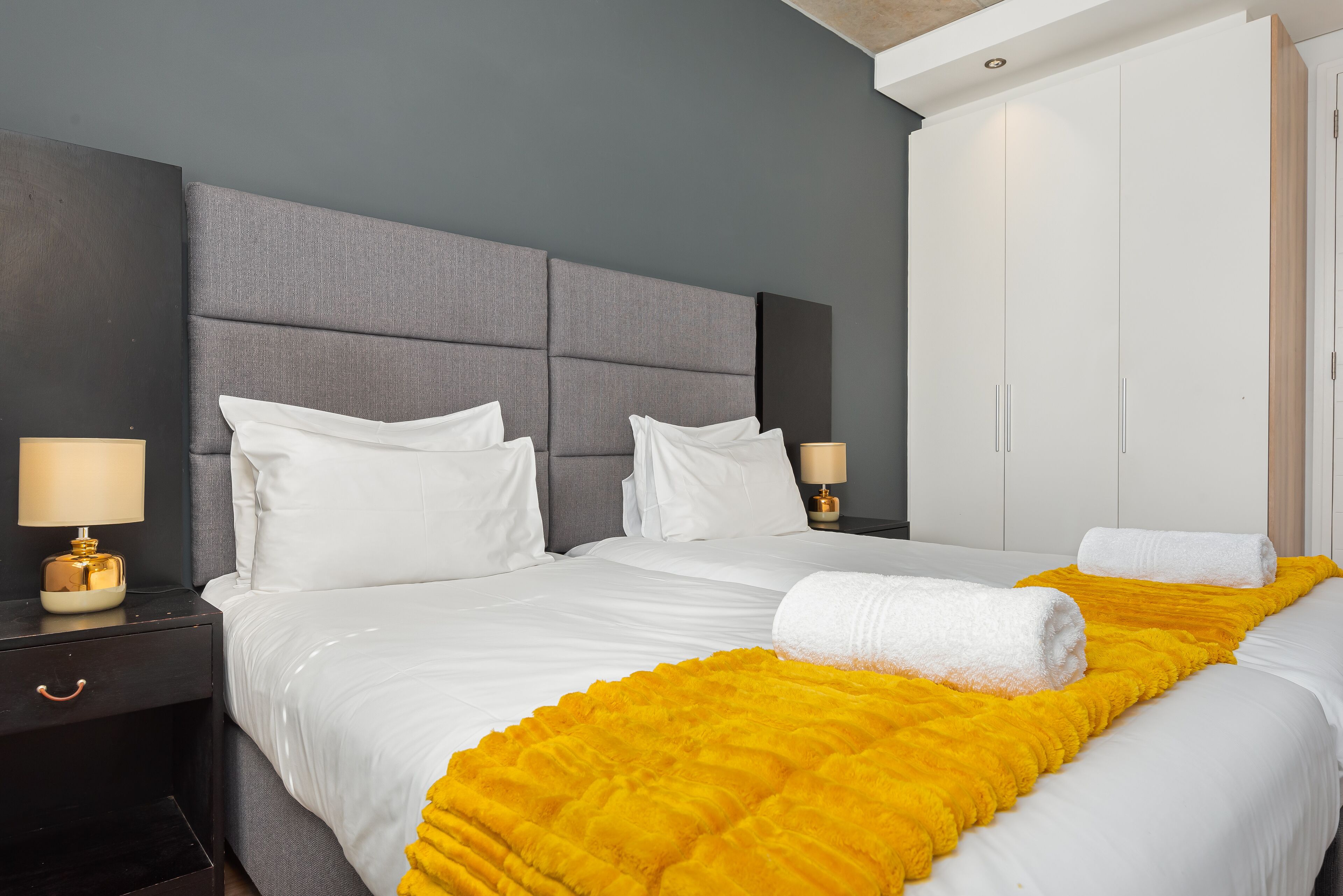 Habitación de hotel con una cama grande, dos mesitas de noche con lámparas, un armario y un edredón amarillo brillante.