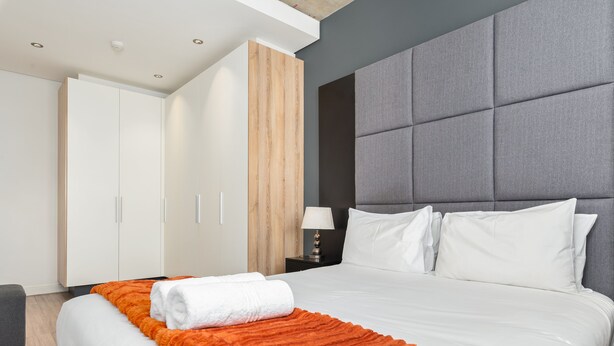 Ein Hotelzimmer mit einem großen Bett, einem grauen Polsterkopfteil, weißer Bettwäsche und einem Holzschrank.