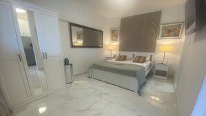 Quarto com cama, mesas de cabeceira, guarda-roupa, espelho e televisão na parede.