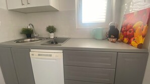 Uma cozinha compacta com máquina de lavar louça, pia, fogão e janela com persianas.