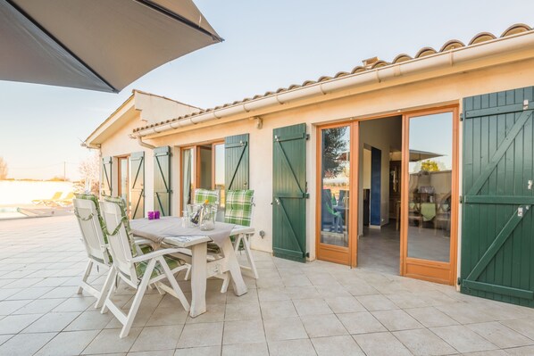A patio area with a table and chairs, a covered seating area, and a building entrance with green shutters.