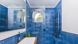 Une salle de bain moderne avec des carreaux bleus, un meuble-lavabo en bois, un lavabo blanc, une cabine de douche en verre et un grand miroir.