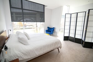 A modern bedroom with a large bed, a chair, and a sliding screen door.