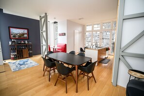 A modern kitchen with a dining area, featuring a large table, red chairs, and a kitchen counter.