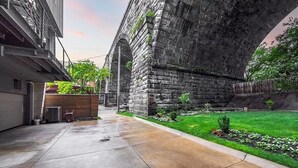 Um pátio com uma ponte de pedra, área gramada e um edifício com garagem.