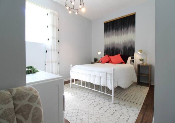 A bedroom with a white bed, red pillows, a white headboard, a nightstand with a lamp, and a patterned rug. - Lake Lovers Paradise (Somerset)