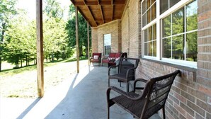 Ein überdachter Patio-Bereich mit Ziegelmauern und großen Fenstern, mit Sitzgelegenheiten im Freien und Blick auf die umliegende Natur.
