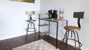 Eine kleine, moderne Küche mit einer Kaffeemaschine, zwei Barhocker und einem Teppich.
