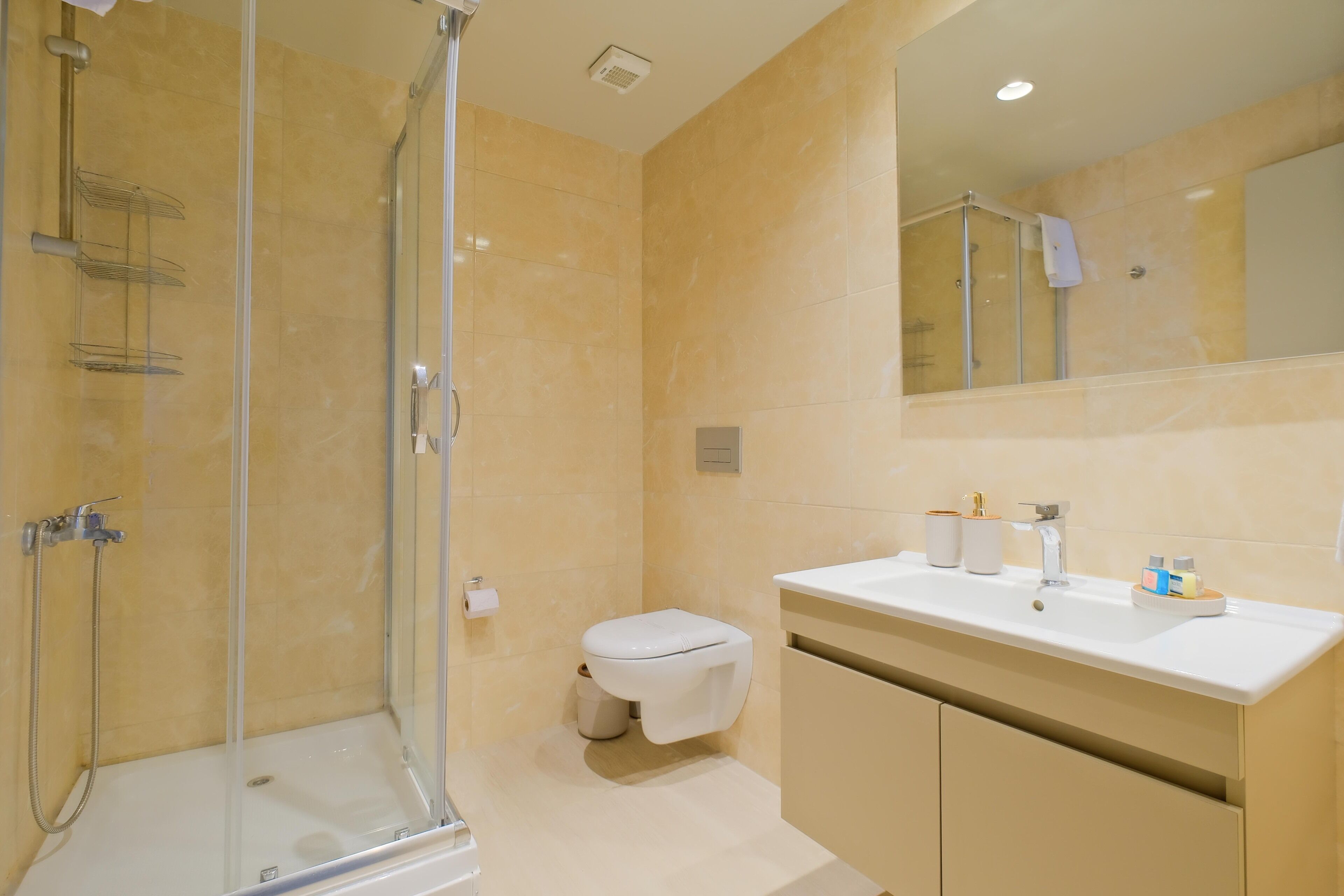 A bathroom with a glass-enclosed shower, a toilet, and a sink with a mirror above it.