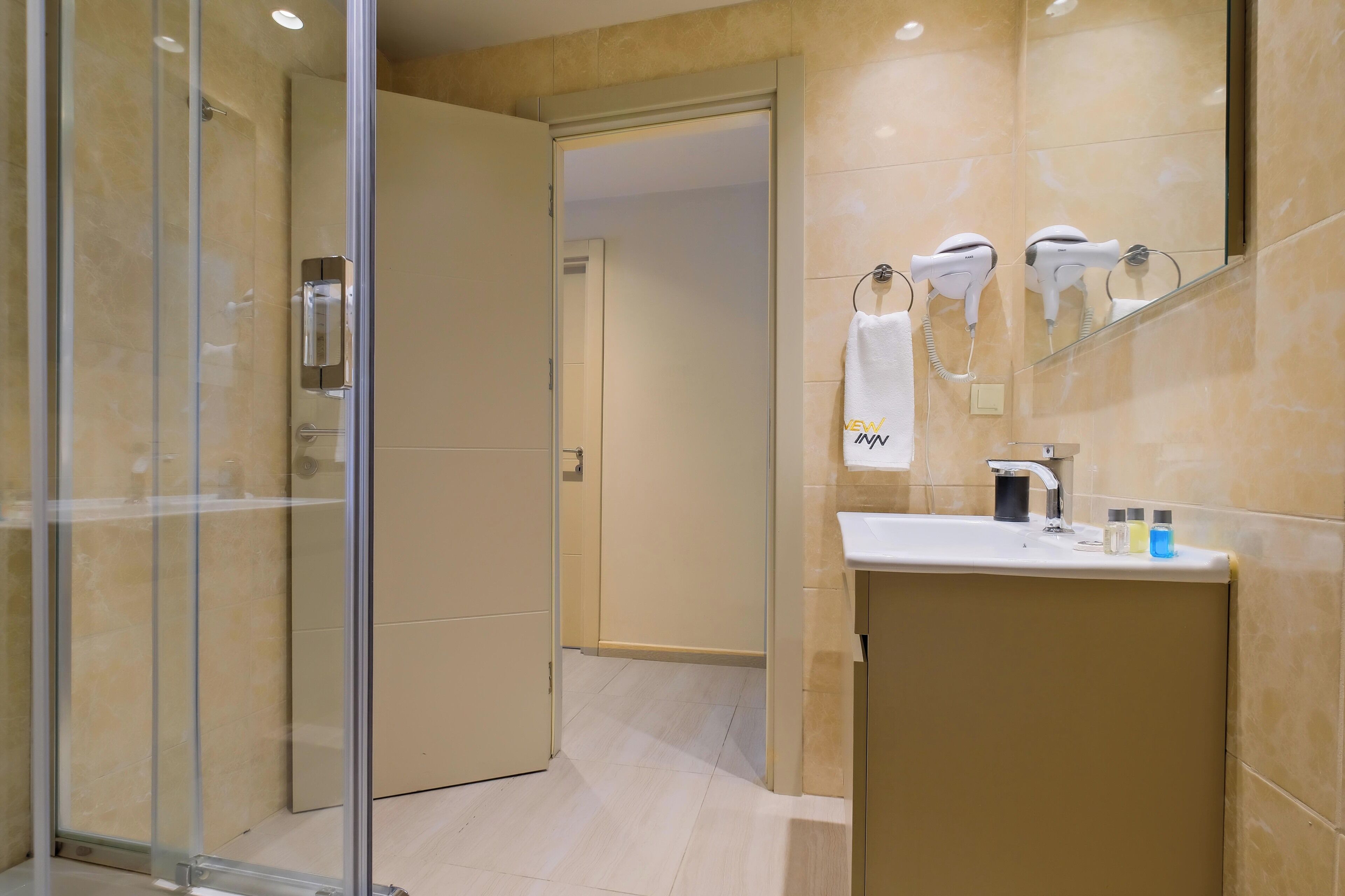 Un baño moderno con cabina de ducha de vidrio, tocador con lavamanos y dos secadores de pelo montados en la pared.