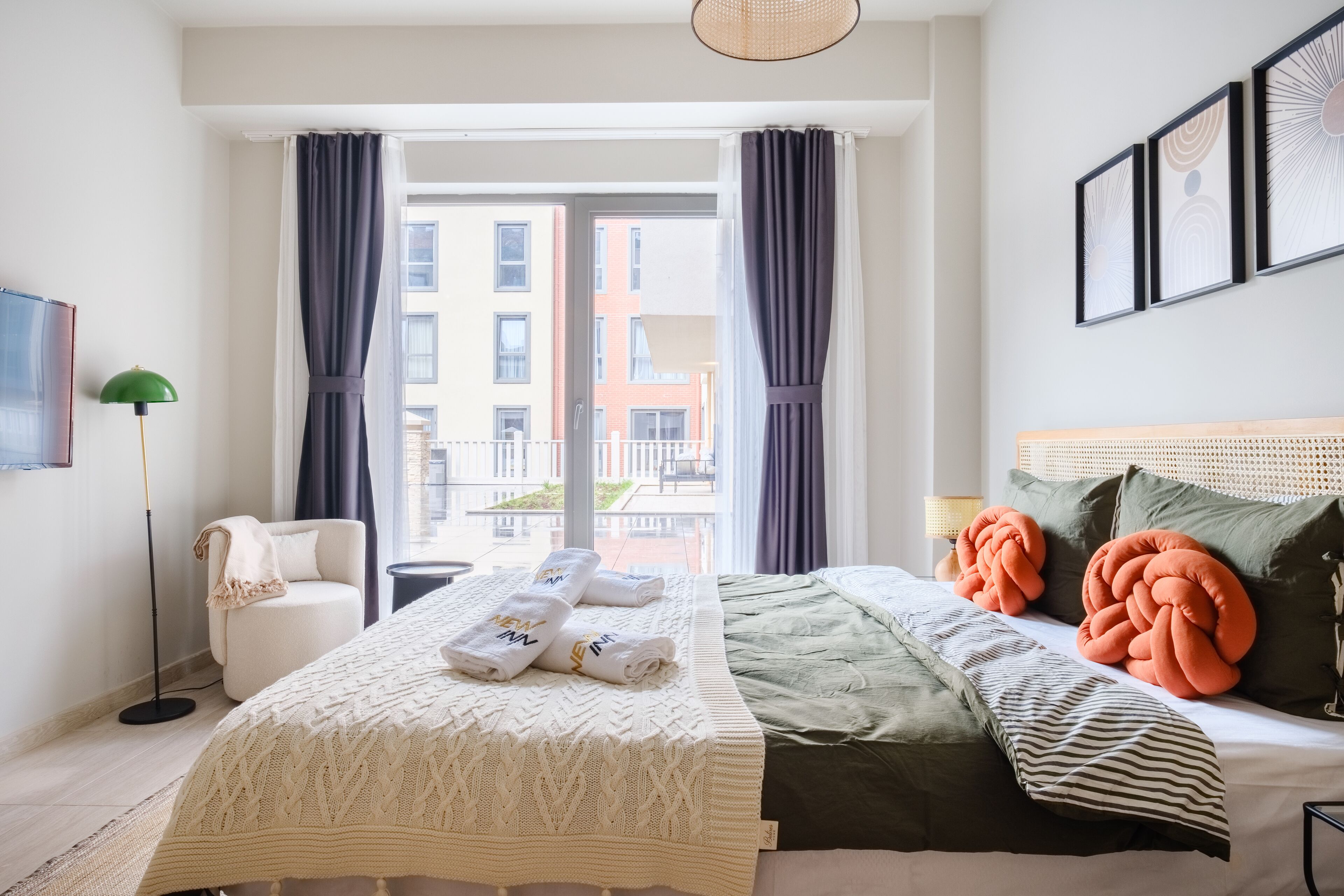 Habitación de hotel con cama, sillón, lámpara de pie y vista al exterior.