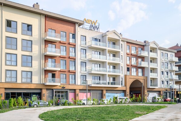 A multi-story hotel with balconies, a central entrance, and a parking area with cars.