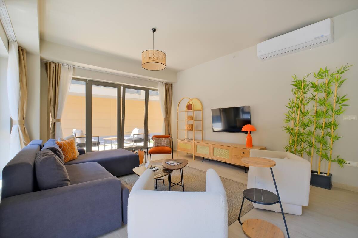 A modern living room with a sofa, armchairs, a TV, and a large window.