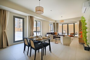 A modern living room with a dining area, large windows, and a view of the outside. - NEW INN Hotel Cadde 54 Mall (Serdivan)