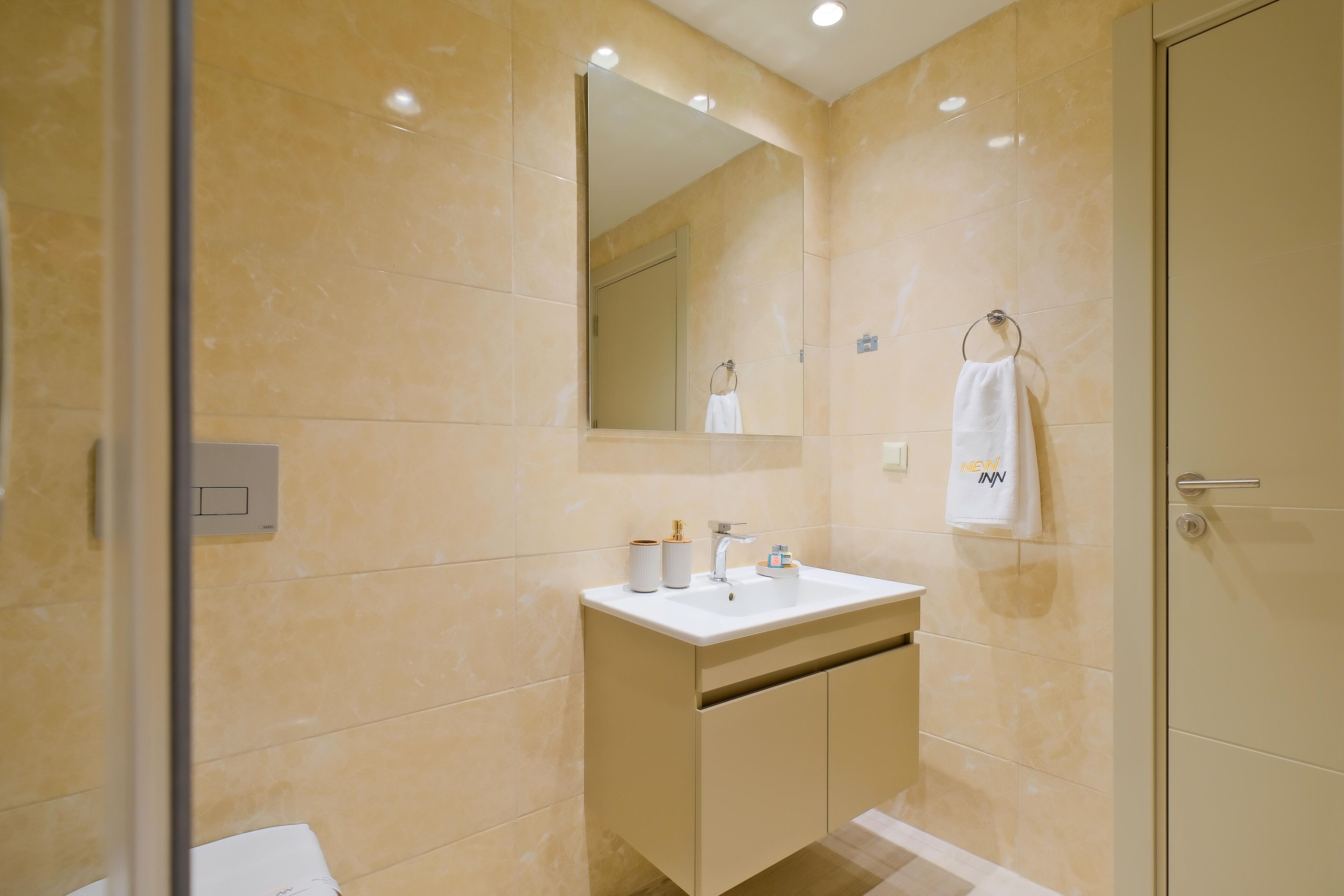 A modern bathroom with a beige marble wall, a white sink, and a large mirror.