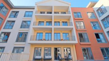 Un immeuble résidentiel à plusieurs étages, doté de balcons, d’une entrée sécurisée et d’un espace extérieur aménagé pour s’asseoir.